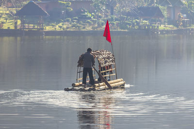 Rear view of man standing in wooden raft on lake