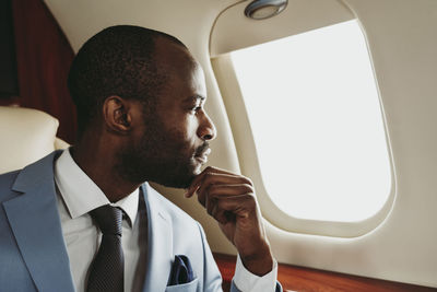 Male entrepreneur with hand on chin looking through window in airplane