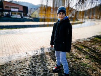 Portrait of boy standing on footpath during winter