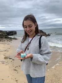 Portrait of young woman standing at beach against sky