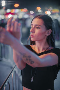 Portrait of young woman standing against illuminated city at night