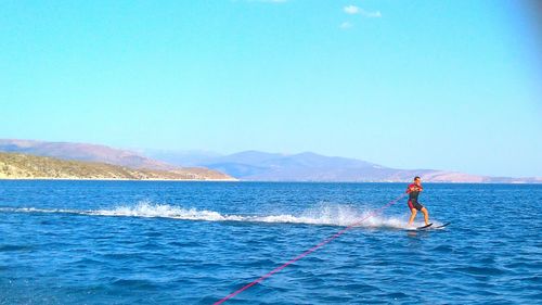 Full length of man waterskiing in sea against blue sky