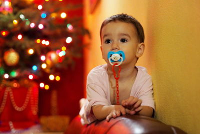 Cute baby boy sulking pacifier while looking away at home during christmas