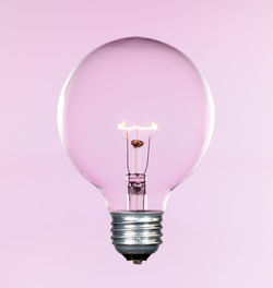 Close-up of illuminated light bulb against pink background