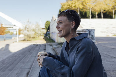 Smiling woman with coffee cup looking away while sitting on steps