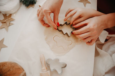 Hands of mom and baby cut out cookies from  dough using metal molds, baking paper