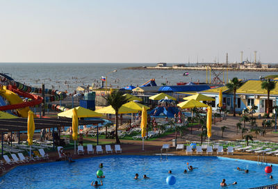 People at swimming pool by sea against clear sky