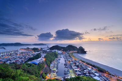 High angle view of illuminated city by sea against sky