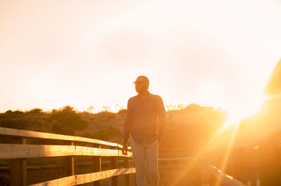 Full length of man standing by railing during sunset