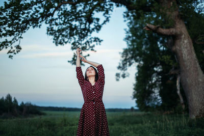 Woman standing by tree on field against sky