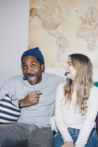 Happy blond woman looking at cheerful man with prop mustache against world map