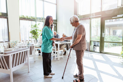 Full length of senior woman shaking hands with healthcare worker at nursing home