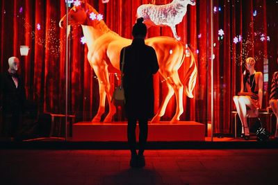 Full length rear view of silhouette woman standing in front of horse sculpture