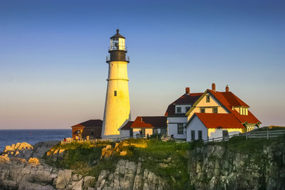 Lighthouse by sea against clear blue sky