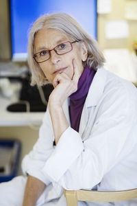 Thoughtful senior female doctor with hand on chin in clinic