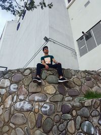 Young man using mobile phone while sitting on building