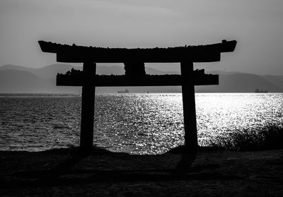 Silhouette wooden post on beach against sky