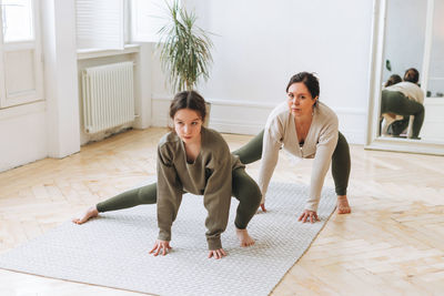 Attractive mother middle age woman and daughter teenager ptactice yoga together in the bright room