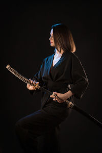 Rear view of woman playing guitar while standing against black background