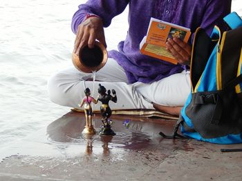 Low section of man pouring water on god figurine at beach