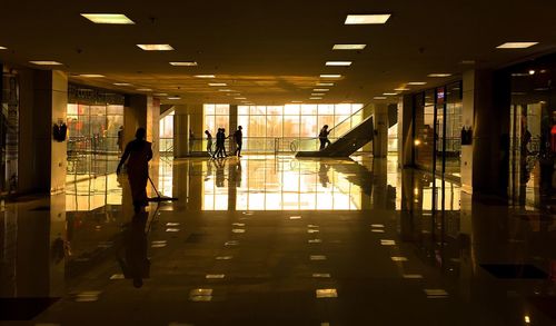 Interior of shopping mall with sweeper cleaning floor and people by escalator