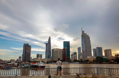 Man standing by river in city against sky