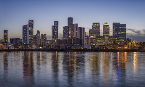 Illuminated buildings by river against sky in city