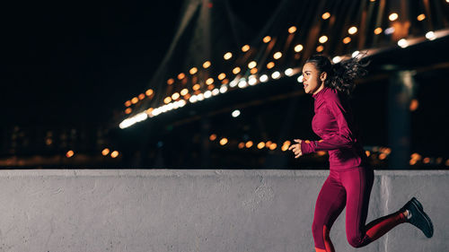 Side view of woman standing against illuminated city at night