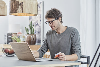 Man holding a card using laptop on table at home