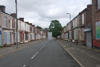 Scenic view of road flaked by buildings against cloudy sky