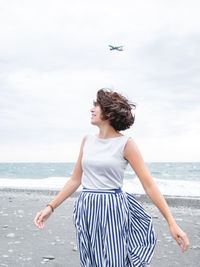 Plane flies in cloudy sky over smiling woman on seaside.  wanderlust concept. vacation on sea coast.