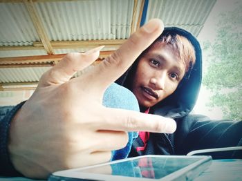 Portrait of young man gesturing peace sign against ceiling