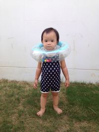 Full length portrait of child standing with inflatable ring in yard by wall