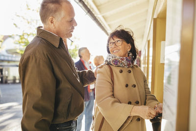 Happy senior woman buying tickets while looking at man at musical theater