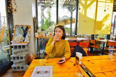 Woman drinking water while sitting on table at cafe