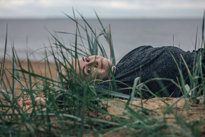 Portrait of young woman relaxing on sand at beach against sky