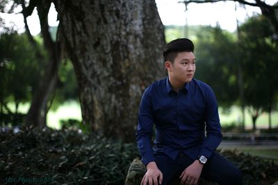 Young man sitting on tree trunk in park