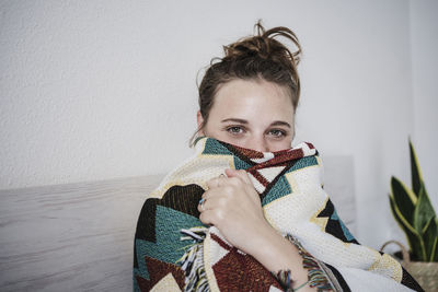 Woman wrapped in blanket staring while sitting on bed at home