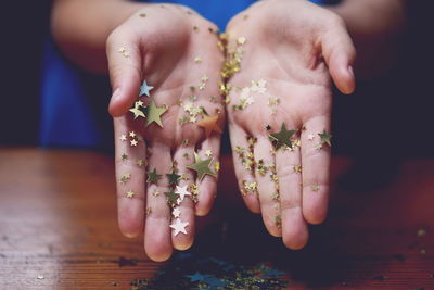 Midsection of person showing golden star shapes on palms over table