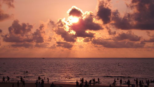 Silhouette people at beach against orange sky