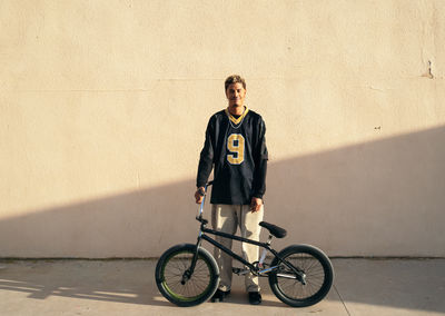 Young ethnic hipster male athlete in cool wear sitting on bmx bike while looking at camera in town on sunny day