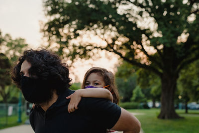 Father giving daughter a piggyback ride, both wearing face masks