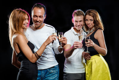 Friends holding champagne flutes while standing against black background