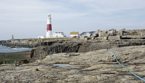 Lighthouse by sea and buildings against sky