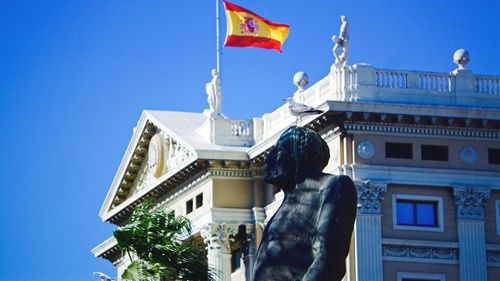 Low angle view of flag against buildings against clear blue sky