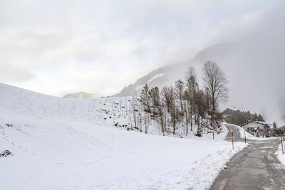 Snow covered road by mountain against sky