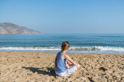 Girl sitting at beach against clear sky