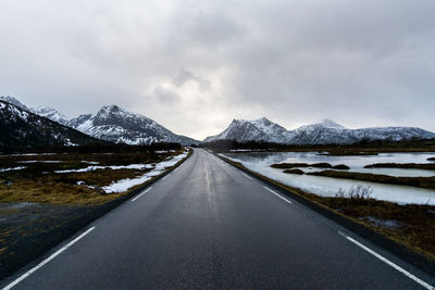 Road leading towards snowcapped mountains against sky