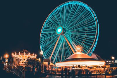 Illuminated ferris wheel against clear blue sky at night