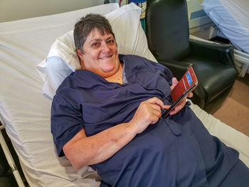 Portrait of female patient using digital tablet while relaxing on bed at hospital